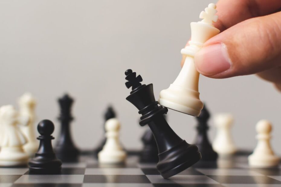 Mão movimentando peça de xadrez branca para capturar o rei preto no tabuleiro, ilustrando estratégia e tomada de decisão no jogo.