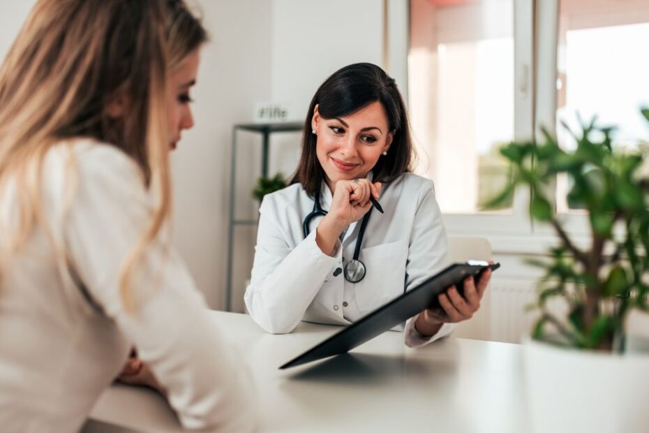 Médica em consulta com paciente em consultório, analisando exames em prancheta e explicando informações de saúde durante atendimento clínico.